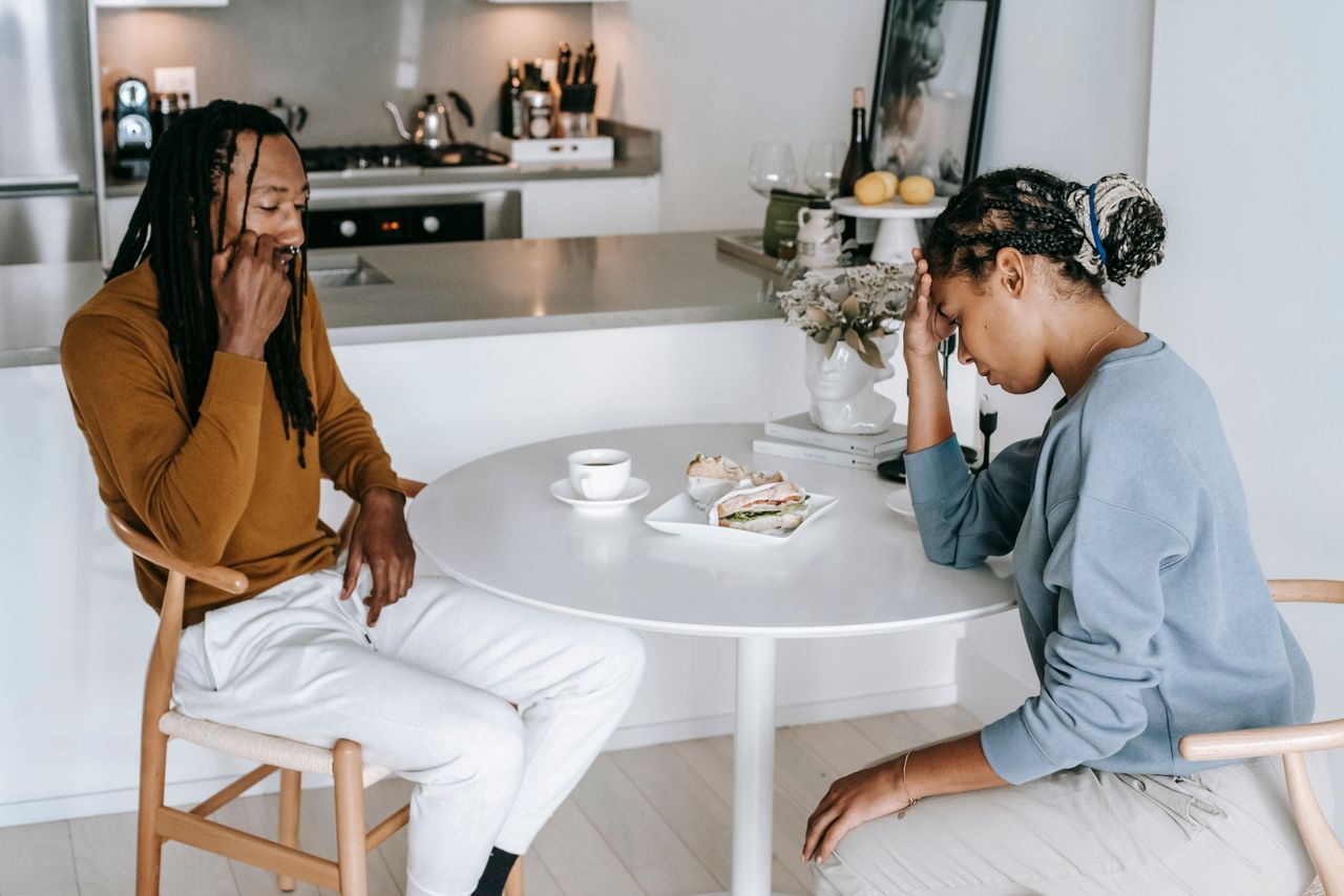 Young black female sitting at table with male and having argument while looking down thoughtfully