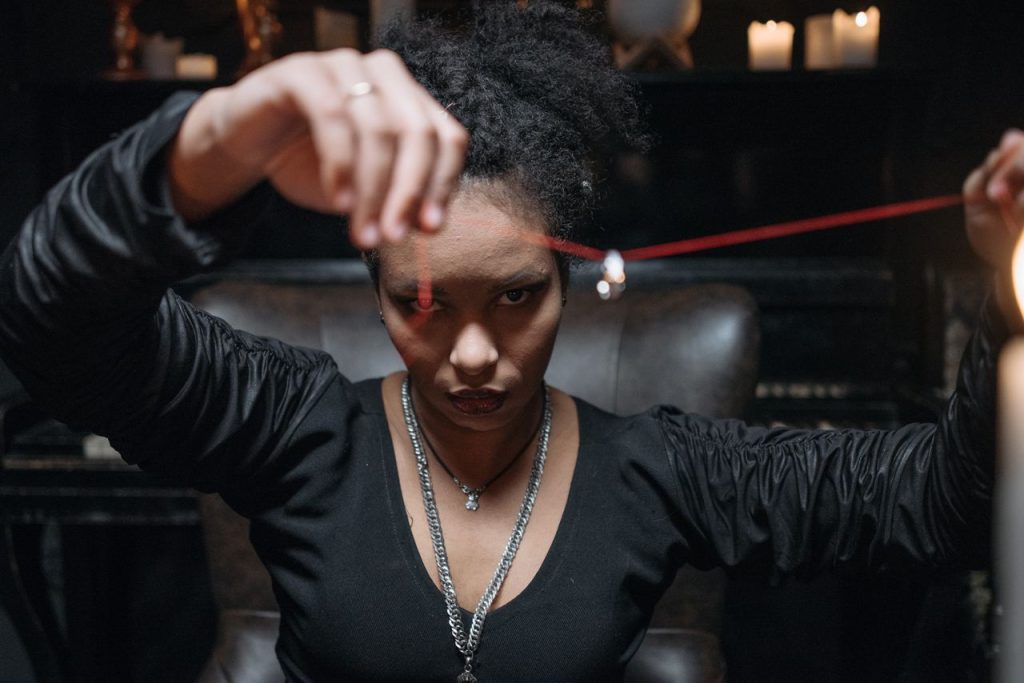 A young woman in a mysterious setting, holding a pendant with intense gaze and dim candlelight.