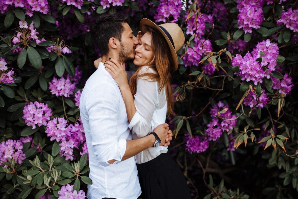pexels-photo-8880448-8880448 A couple sharing an intimate moment surrounded by vibrant purple rhododendron flowers.