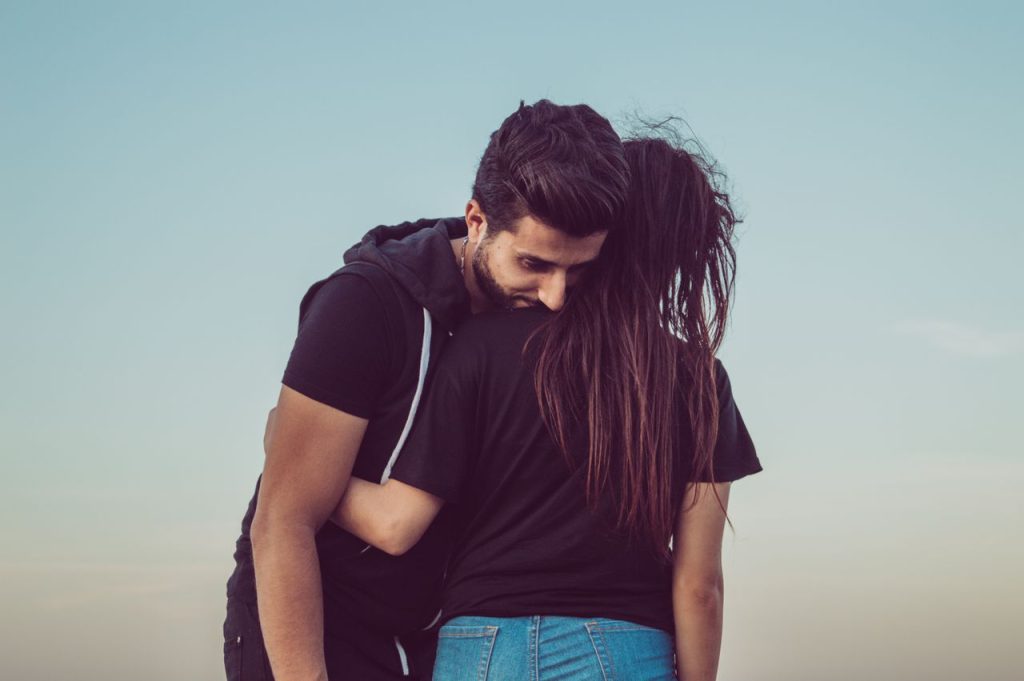 A romantic moment of a young couple hugging outdoors against a serene sky.
